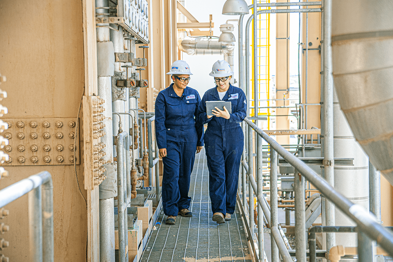 Two employees walking in an industrial facility and looking at a tablet.