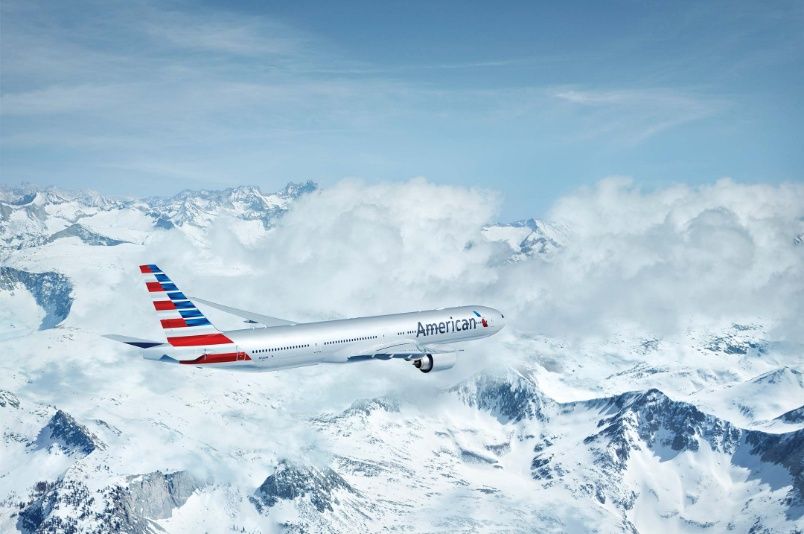 An American Airlines plane flies over a beautiful, snowy mountain range