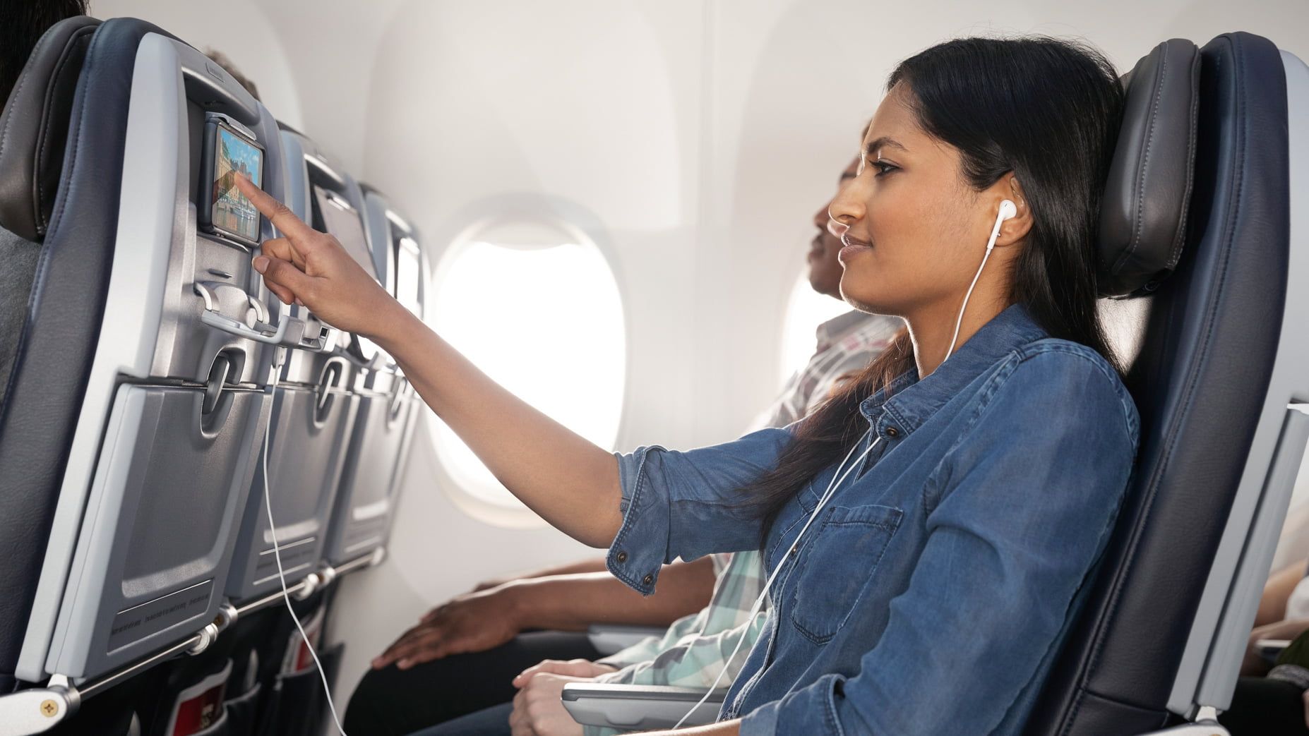 A woman kicks back in her airplane seat and queues up some in-flight entertainment