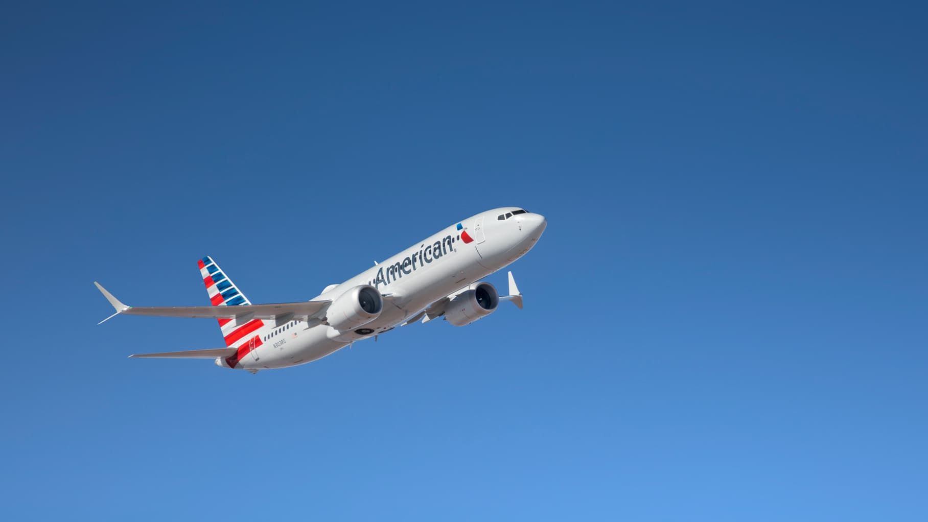 An American Airlines plane flying in against a clear blue sky
