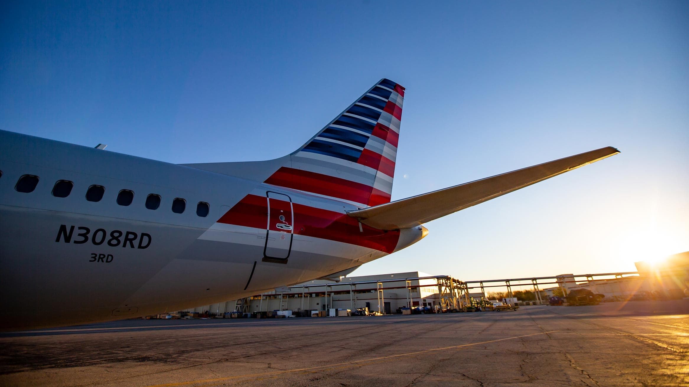 Close-up of an airplane's tail fin and wing in the sky, with clear, sunny skies in the background