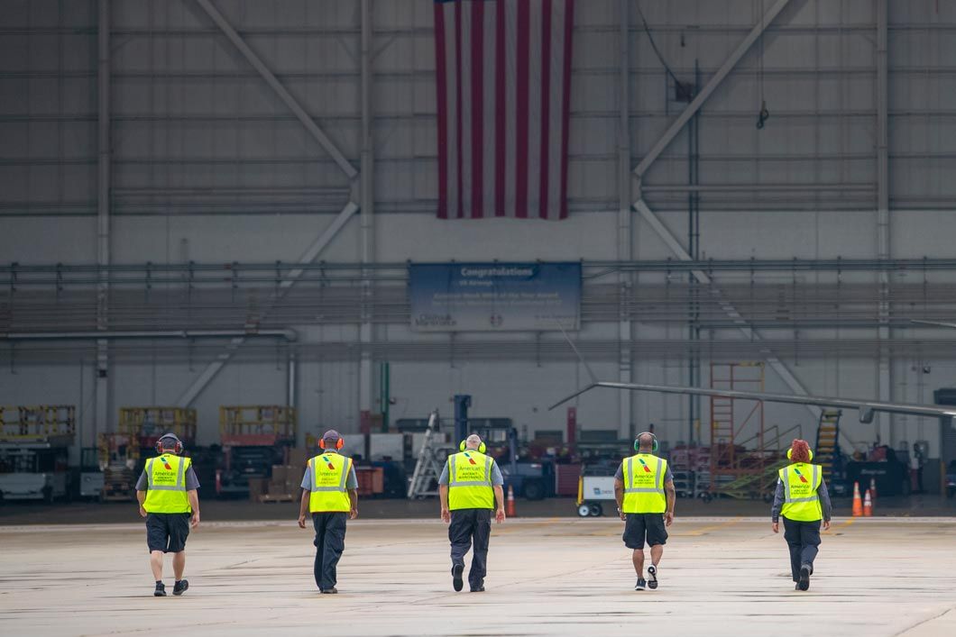 Five American Airlines workers in bright yellow safety vests walk towards a hangar