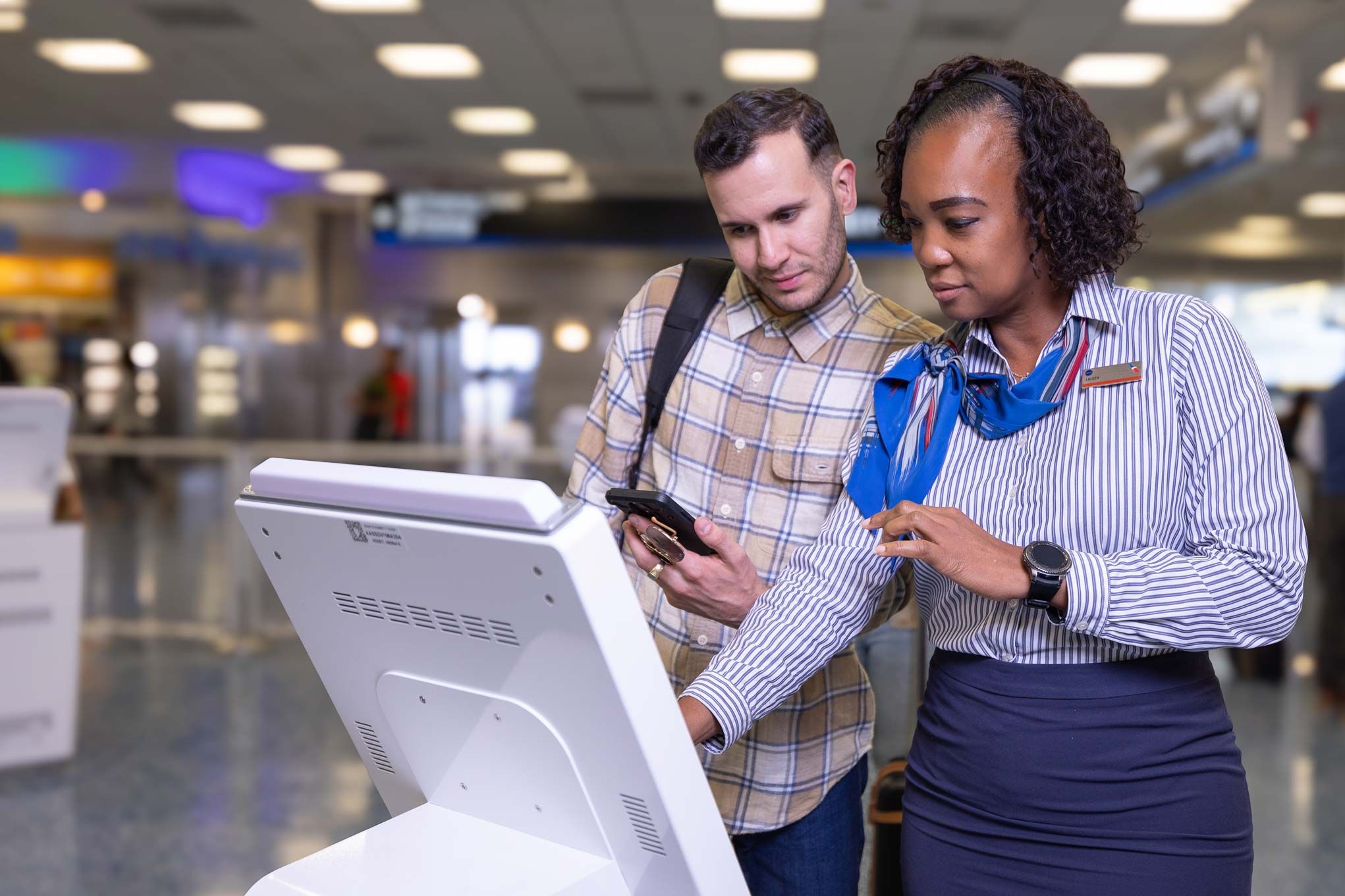 An American Airlines desk agent assists a customer with a digital kiosk